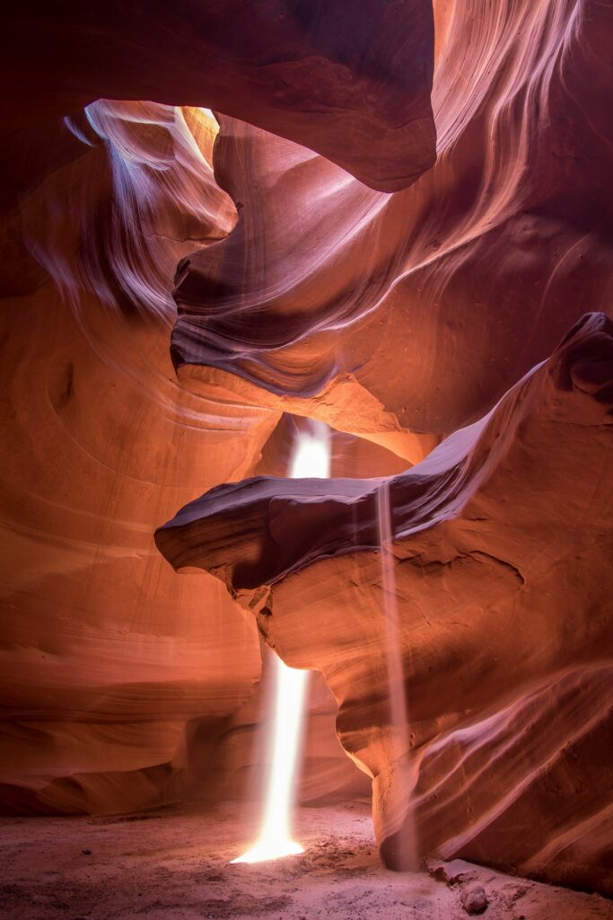 Sonnenstrahlen fallen durch eine Öffnung in die geschwungenen, orange-violett schimmernden Felswände des Antelope Canyon in Arizona